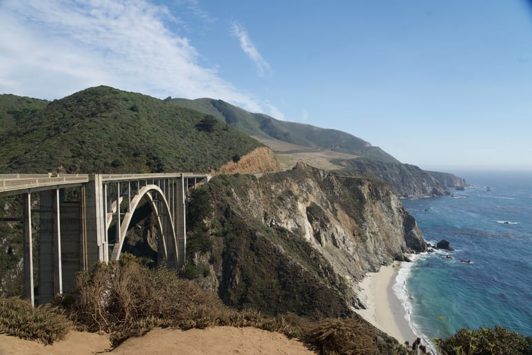 Arched concrete bridge spanning a rocky coastal ravine above the ocean