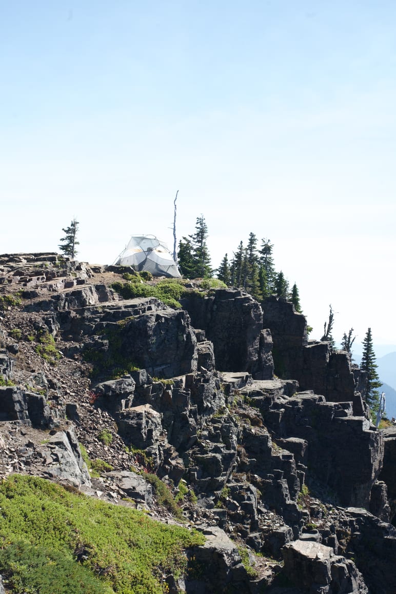 A dome tent pitched on a rocky ridge among wind bent trees