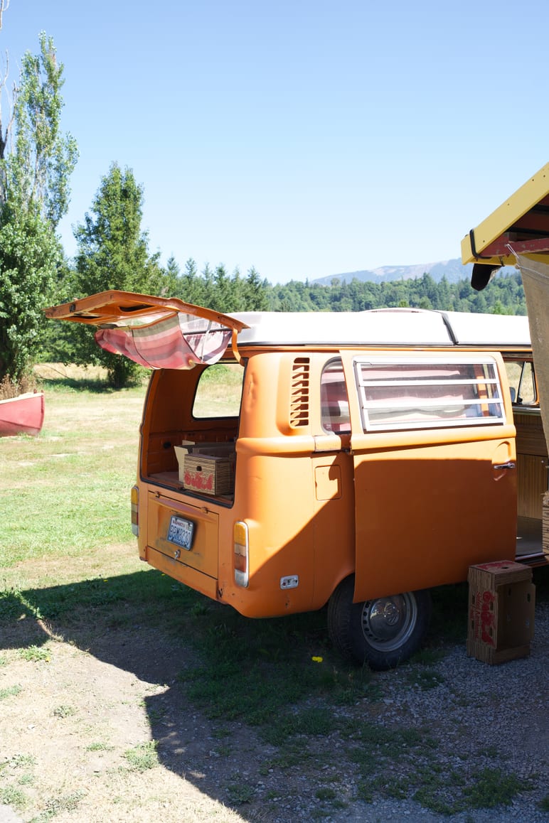 A vintage orange van sits parked in a grassy field on a sunny day