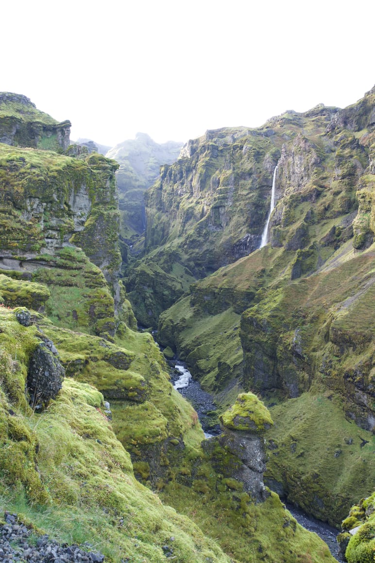 A distant waterfall drops through a deep mossy canyon
