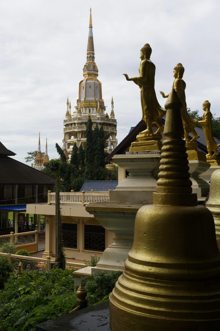 Golden temple spires and Buddha statues rising against a cloudy sky