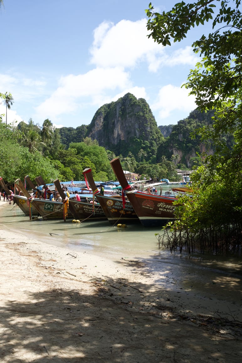 Wooden longtail boats moored on a beach beneath a tall limestone peak