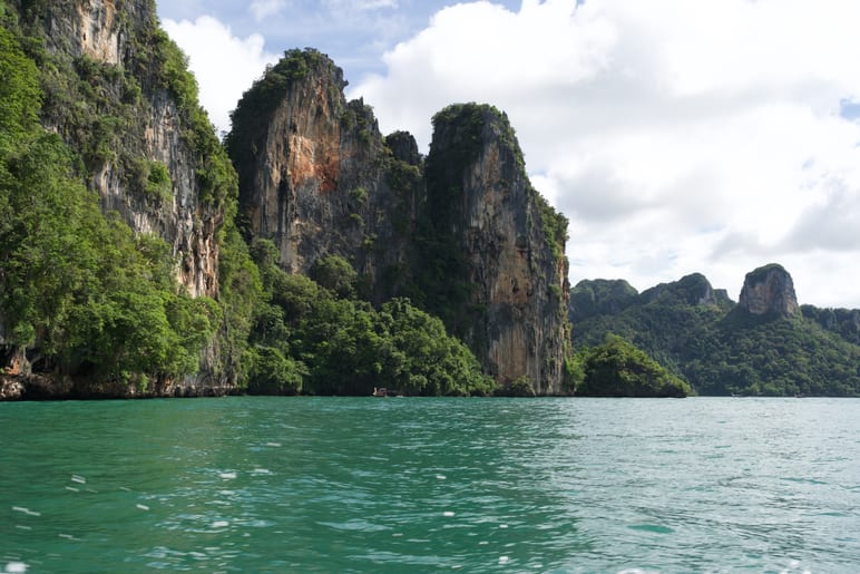 Turquoise water below tall, jungle covered limestone cliffs