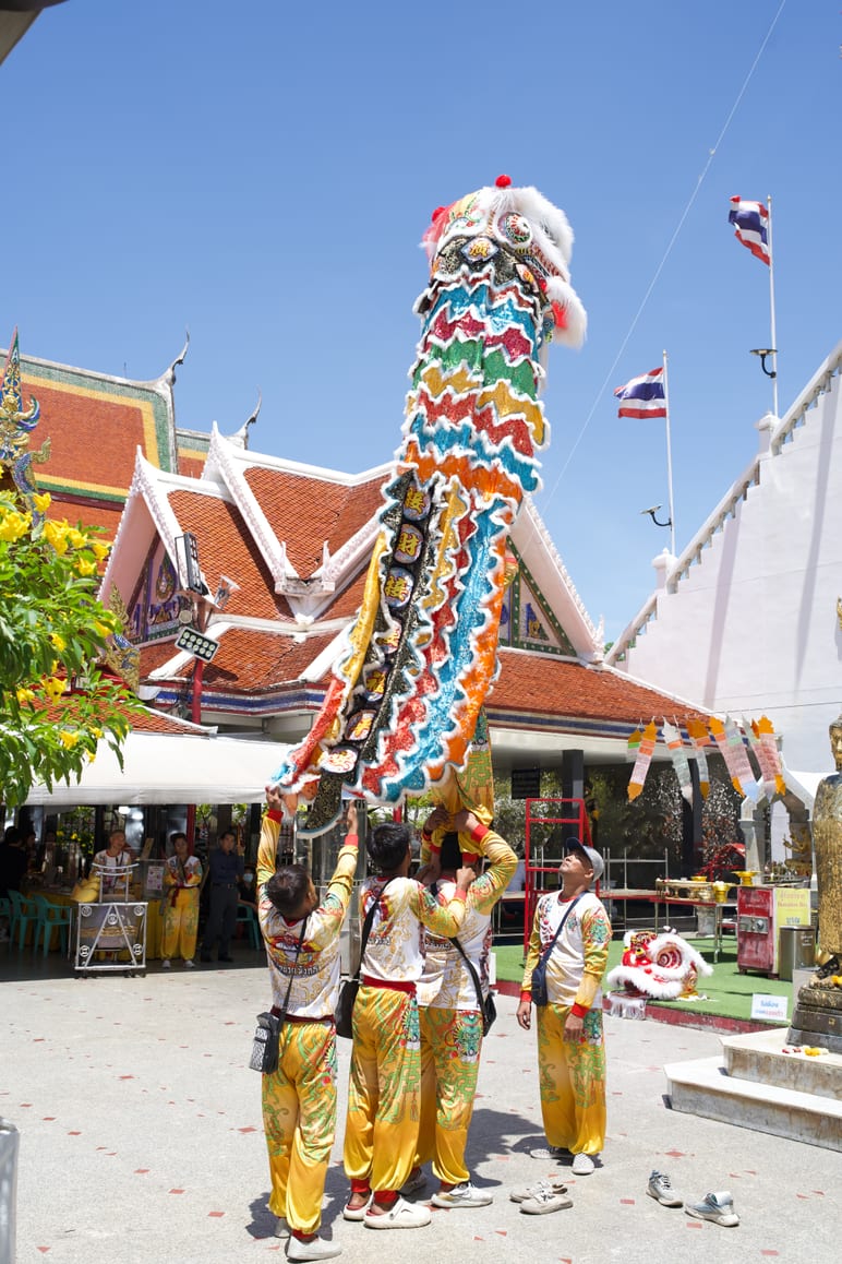 Performers hoisting a long dragon costume on poles in front of a temple roof