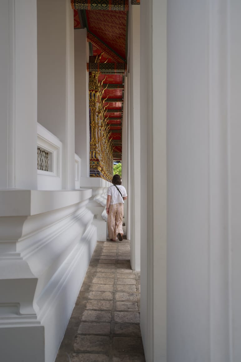 A person walking down a long, ornately painted covered temple corridor