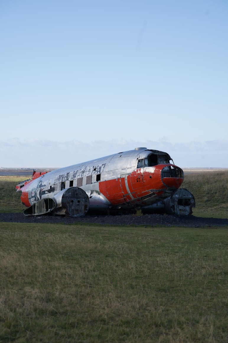 A weathered plane fuselage rests in a grassy field under clear sky