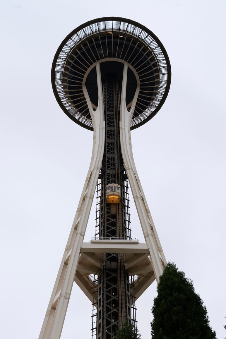 Looking up at a saucer shaped tower with an elevator car climbing its legs