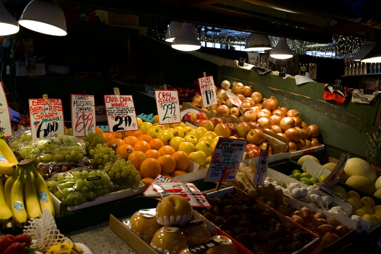 Market stall overflowing with citrus, grapes, and onions under hanging lamps