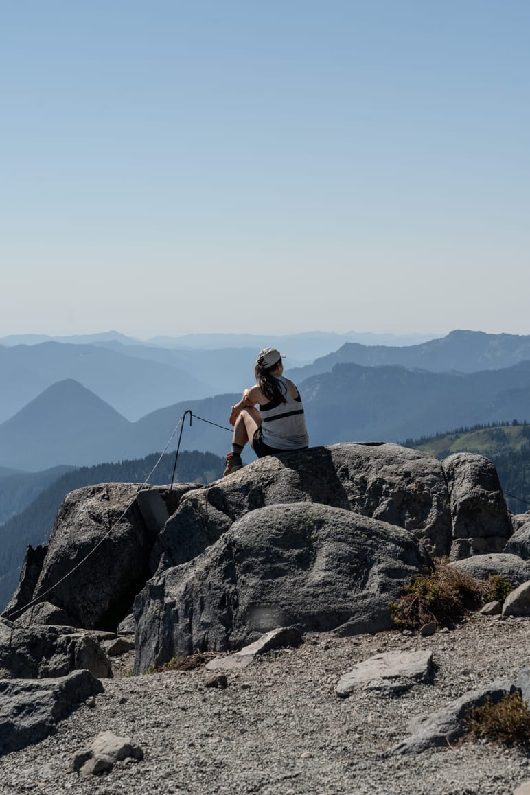Hiker sitting on a rocky outcrop gazing across layered mountain ridges