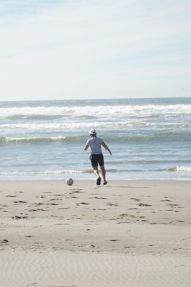 A person kicking a soccer ball along the shore as waves roll in