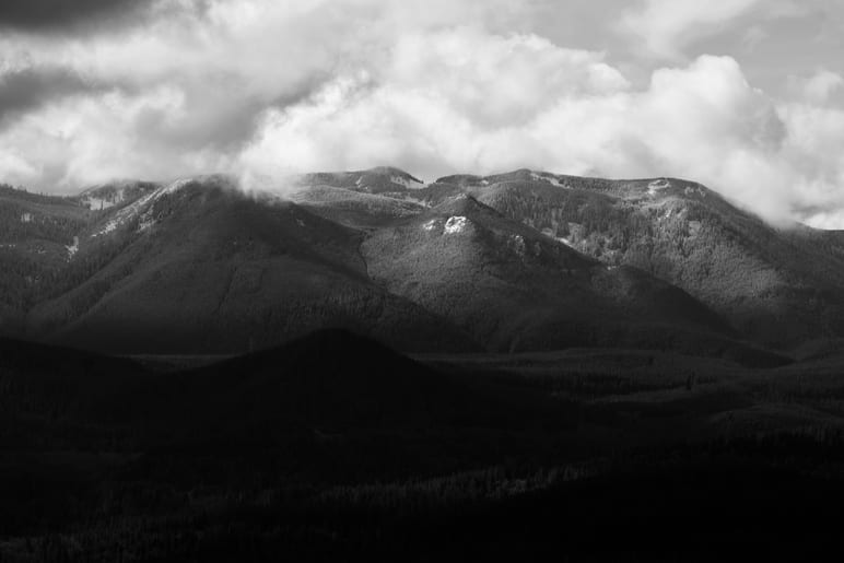 Layered mountain ridges in black and white beneath a cloudy sky