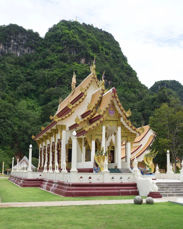 Ornate temple with a layered roof set against a forested limestone cliff