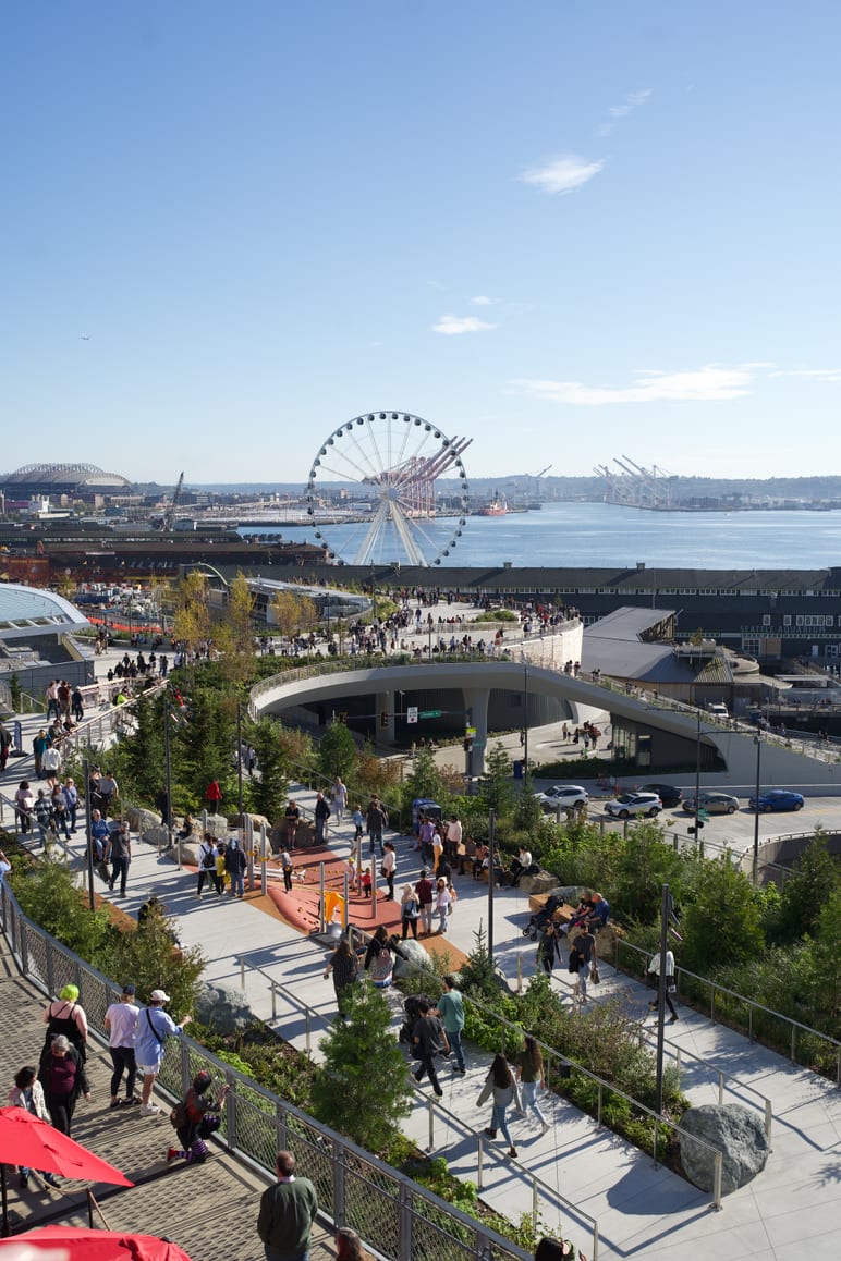 Elevated waterfront park with a ferris wheel and crowds overlooking the harbor