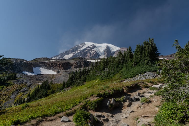 Snow-capped mountain peak wreathed in cloud above a green alpine meadow