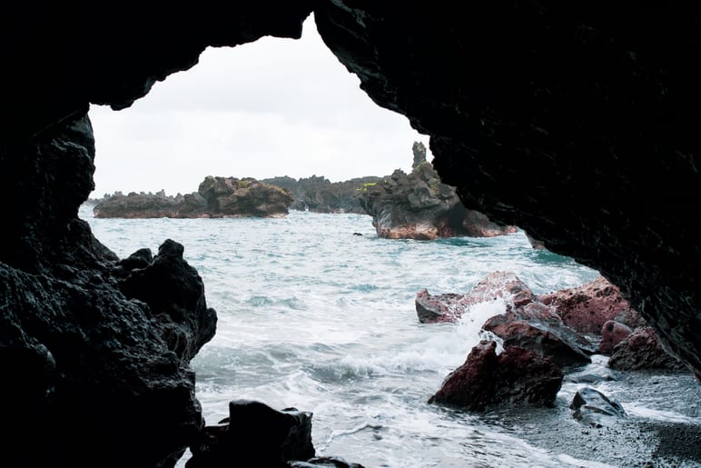 View through a dark sea cave opening toward rocky islets