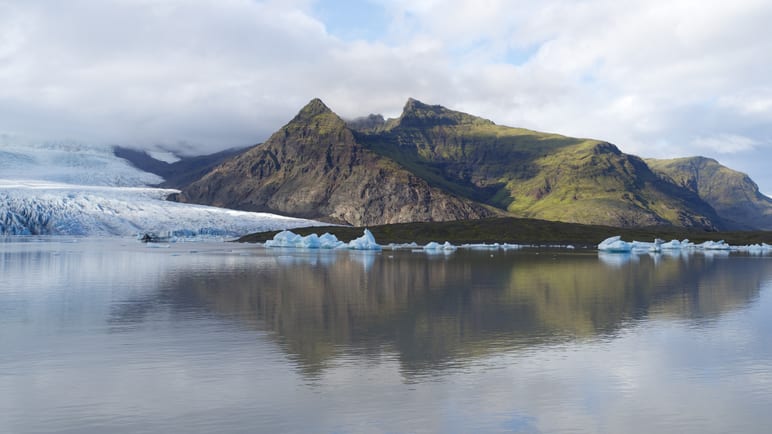 Icebergs float in a still lagoon before a glacier and mountains