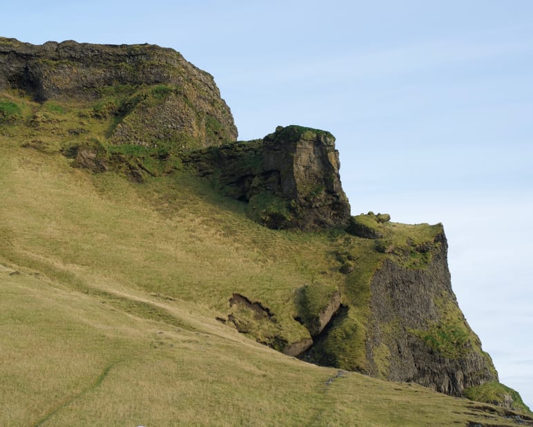Layered mossy cliffs rise above a grassy slope