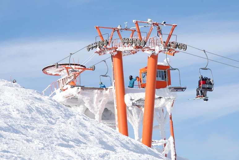 Snow and ice coat the towers of a ski lift under blue sky