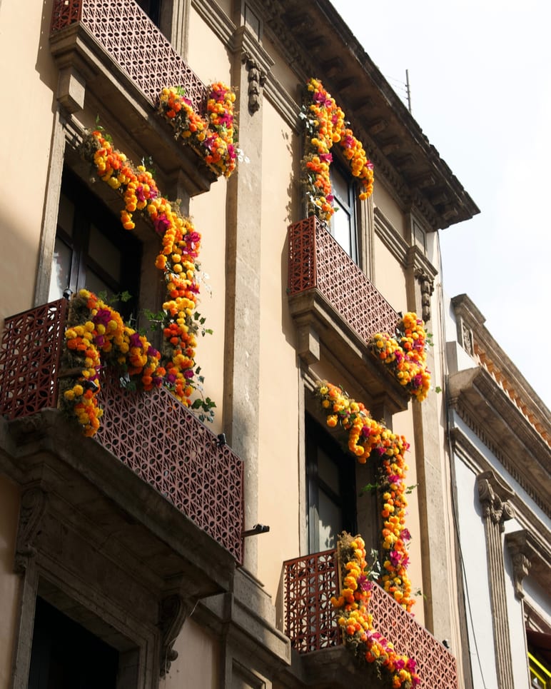 Building facade draped in orange and yellow flower garlands down iron balconies