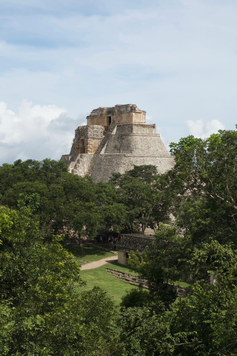 Stepped pyramid rising above a canopy of trees under a partly cloudy sky