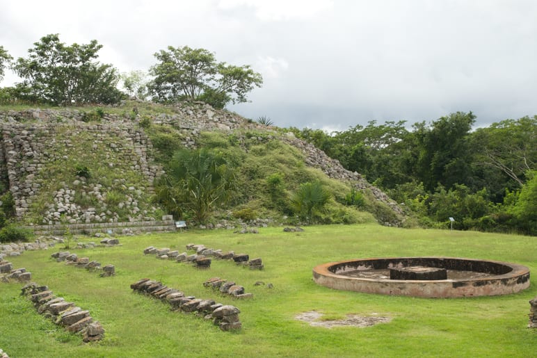 Stepped stone pyramid ruins beside a circular platform, overcast sky above
