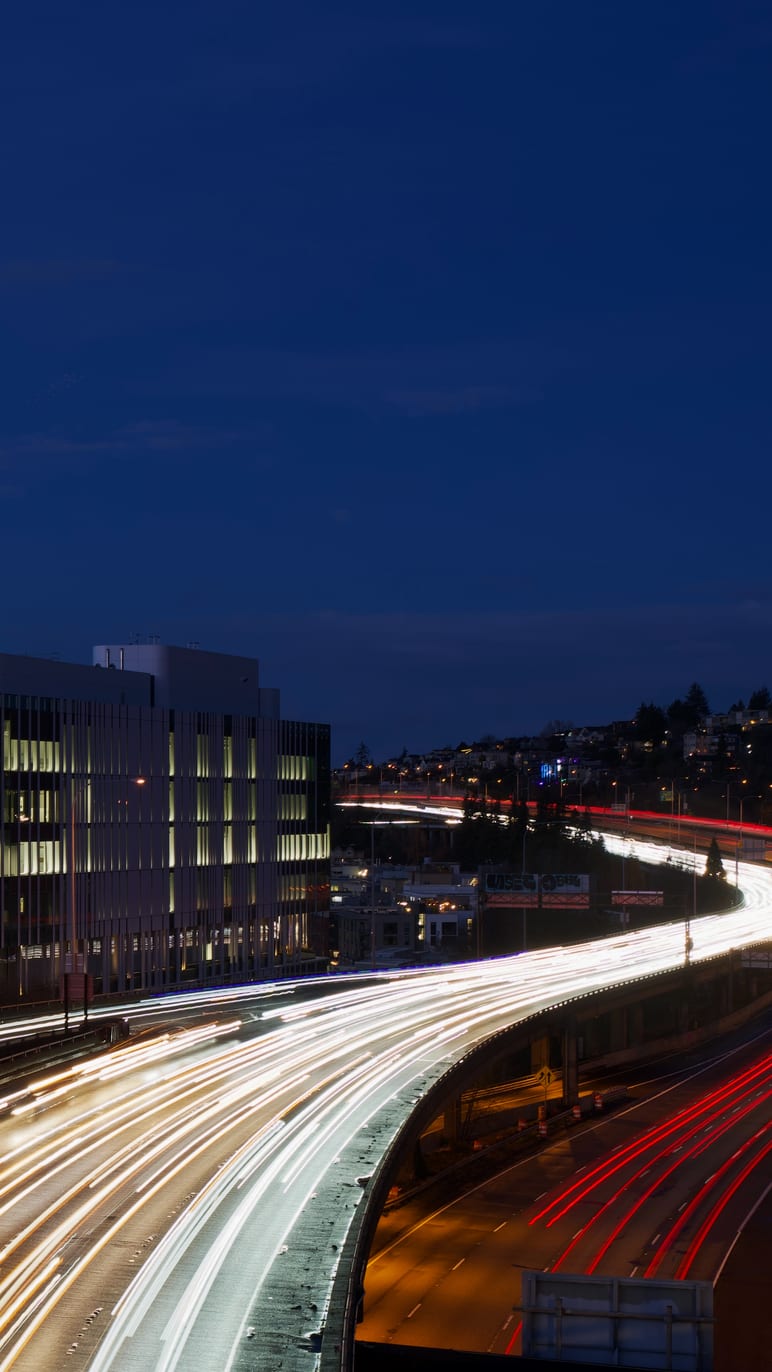 Long exposure light trails streak along a curving highway at night
