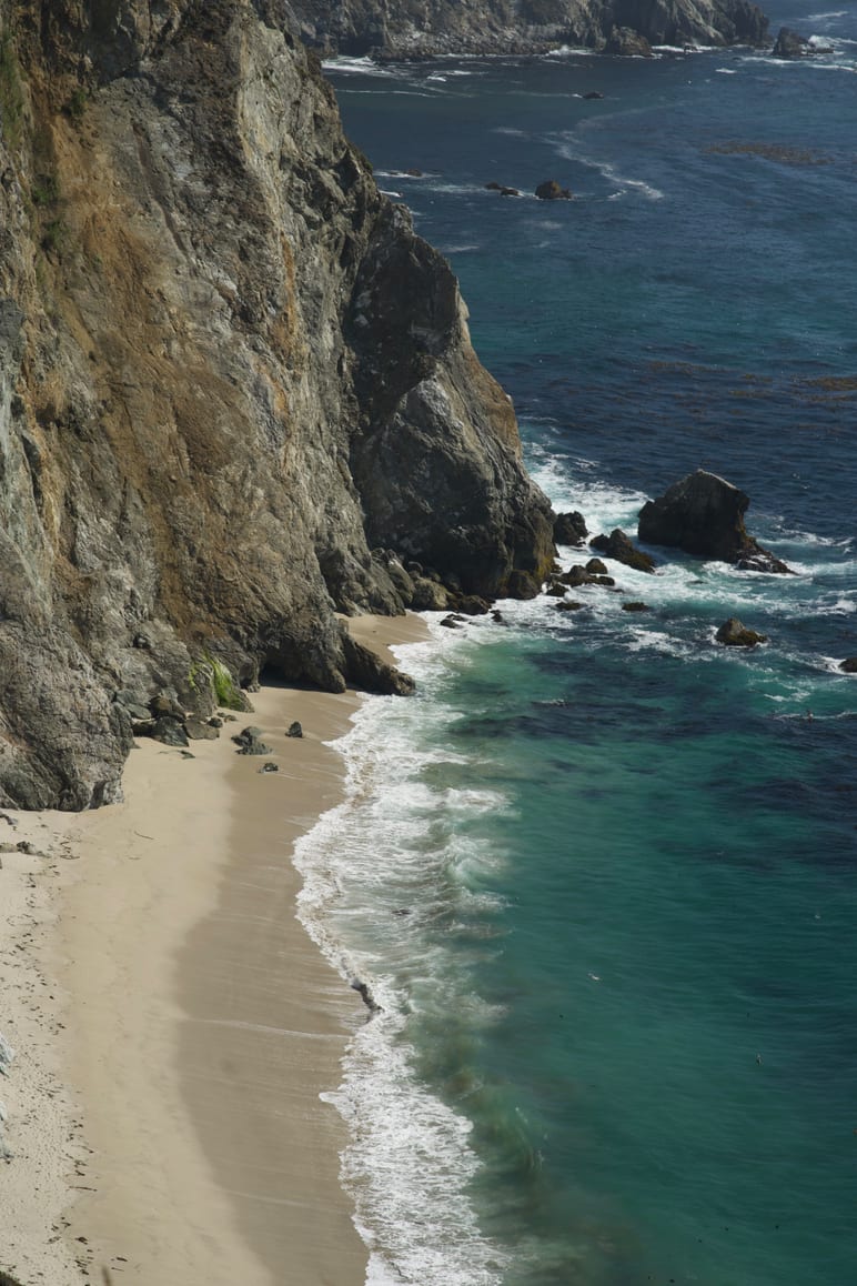 Steep cliffs dropping to turquoise water and a narrow crescent of sand