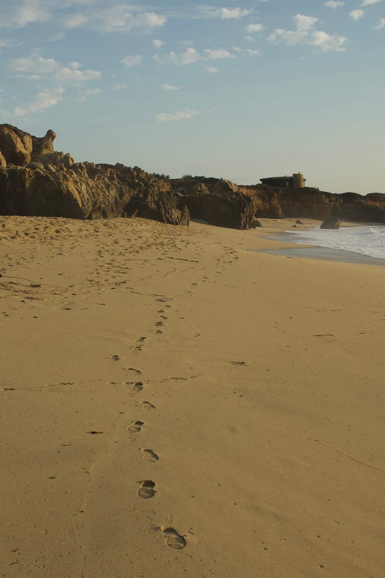 Footprints trailing across a sandy beach toward rocky cliffs in warm light