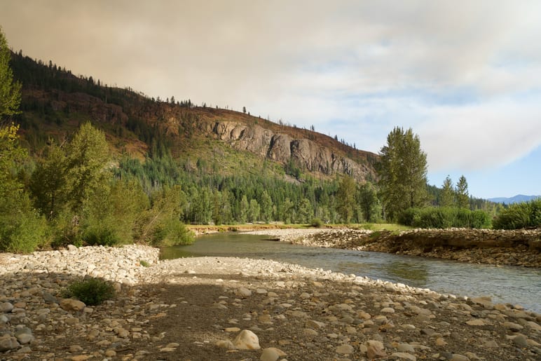 Wide river bend curving beneath a forested ridge under a hazy sky